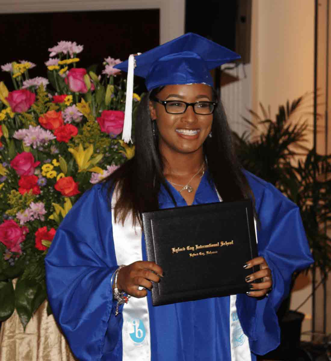 Grad in cap and gown posing and smiling with diploma